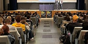 Ricci e Dionigi sul palco e ragazzi a sedere in platea, con nello sfondo Gianfranco Gaudiano