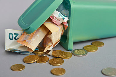 Soldi in carta e spiccioli che escono da un bidoncino verde