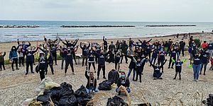 Gruppo di persone Morotti Angeletti in spiaggia con sacchi neri 