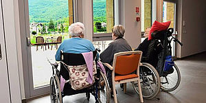 Anziani in carrozzella che guardano fuori da una vetrata